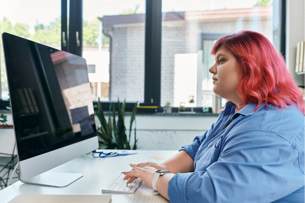 Woman with pink hair concentrating on a computer