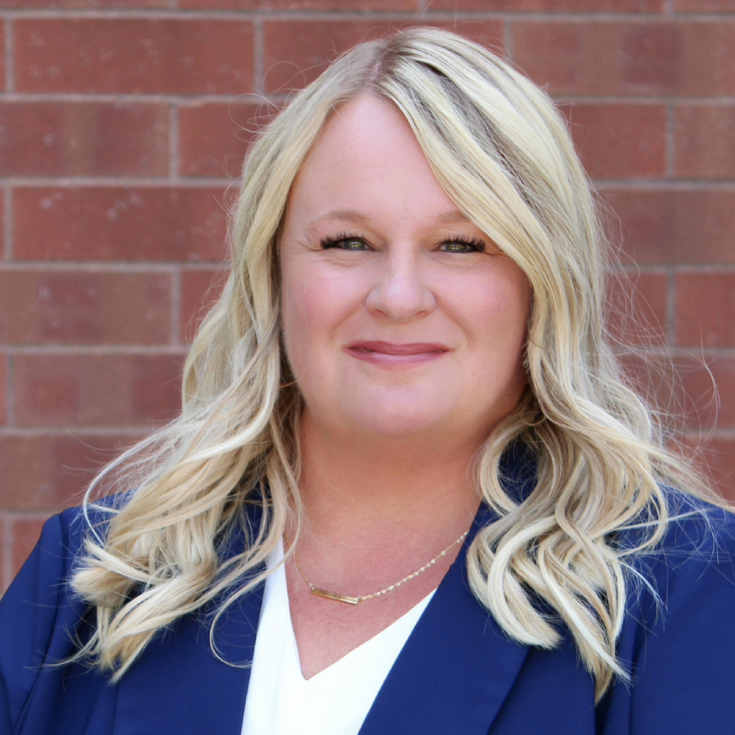 Shana Stenberg, a blonde woman in a white shirt and blue blazer, against a brick wall